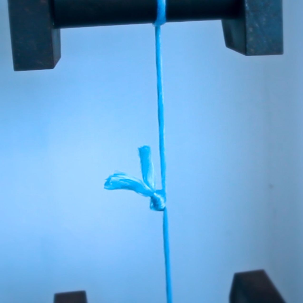 Blue string tied in a knot between two vertical clamps against a soft blue background.
